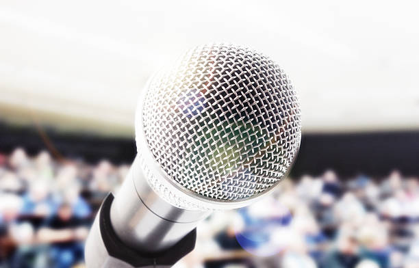 istock Vocal microphone in front of defocussed lecture or meeting audience 485136072