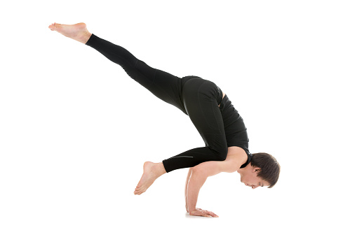 Sporty young man working out, doing arm balancing handstand yoga asana, One Legged Crane Pose, Half Crow Pose, Eka Pada Bakasana on white background