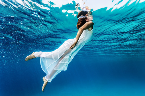 Nice girl emerges from the sea, swimming underwater, enjoying nice refreshing water, wearing long dress, summer vacation and travel concept