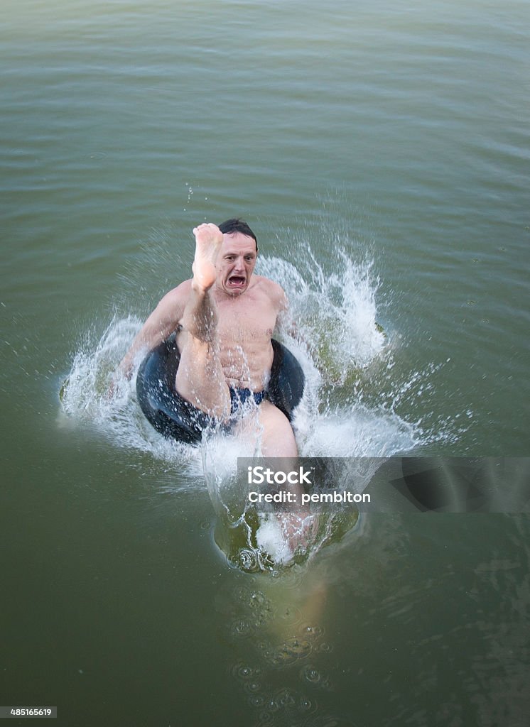 Splosh! Funny image of a men jumping into the water on tire. Lake Stock Photo