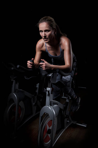 Female Athlete Cycling in Gym Young and attractive woman is cycling in the gym. spin bike stock pictures, royalty-free photos & images