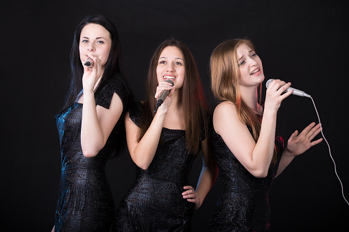 Group of three emotional beautiful young female singers with microphones singing, girls band concert