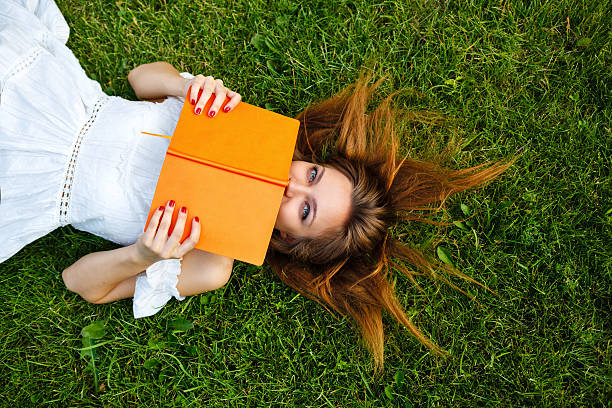 Close up of a woman hand writing on a notebook outdoor lying on the grass in a park