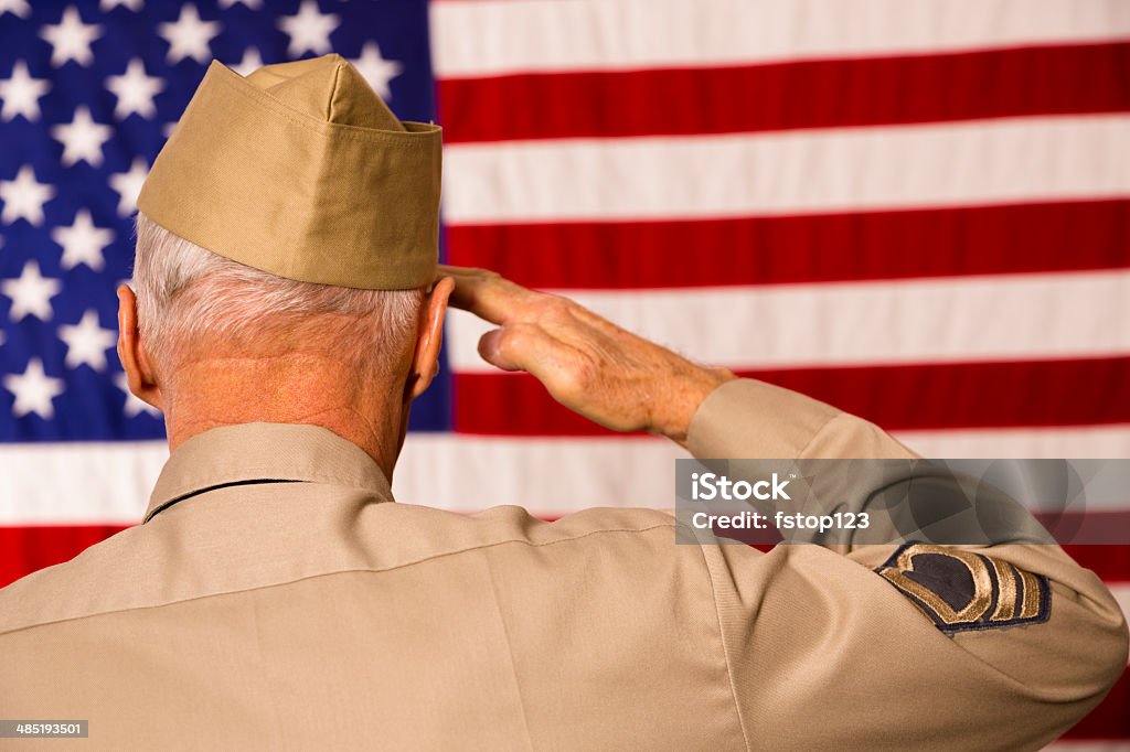 Military: Senior veteran in uniform saluting American flag. Senior man, army veteran saluting the USA flag.  He wears a WWII military uniform.  Patriotism. Veteran Stock Photo