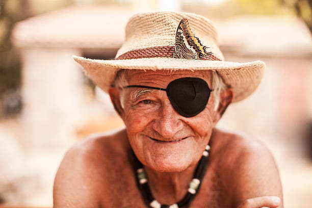 Portrait of old man with eye patch Portrait of old man with eye patch. Photo taken outdoors, at cloudy day with soft daylight. Man is shirtless, looks very happy and wearing old hat. During the photoshooting, one beautiful butterfly landed on his hat one eyed stock pictures, royalty-free photos & images