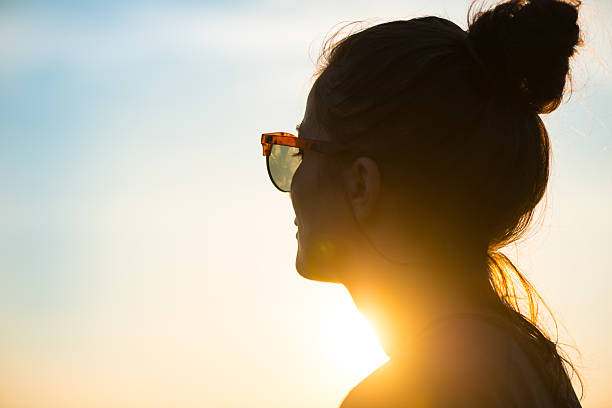 mujer joven lleva gafas de sol mirando al atardecer - contraluz fotos fotografías e imágenes de stock