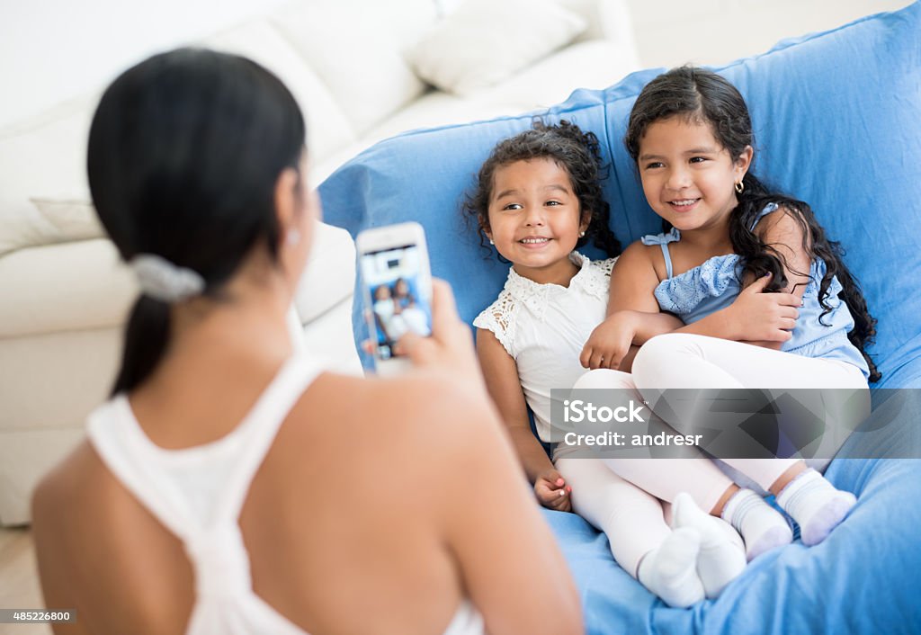 Mother taking a picture to her daughters Latin mother taking a picture to her happy daughters at home with a cell phone 2015 Stock Photo