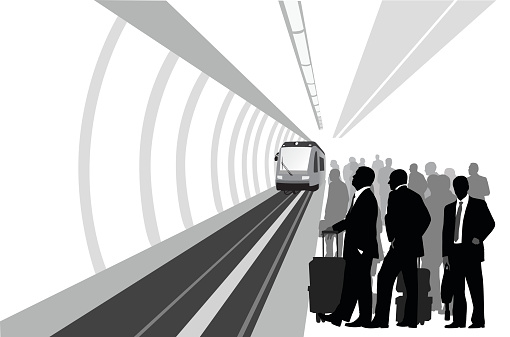 A vector silhouette illustration of business men waiting to commute to work on the train.  They stand in a crowded train station where there is an approaching train.
