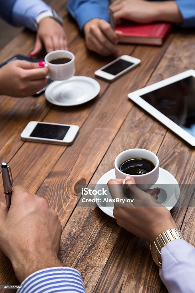 Informal business meeting Wooden cafe desk and hands of people drinking coffee with many electronic devices business style dress code male and female telephones tablets PC Cafe Stock Photo