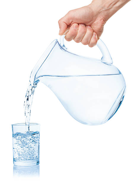 Water poured from the pitcher into a glass. Water poured from the pitcher into a glass, isolated on the white background, clipping path included. blue jug stock pictures, royalty-free photos & images