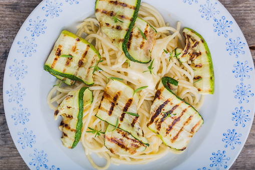 Pasta with grilled zucchini, cheese and fresh thyme on a white plate