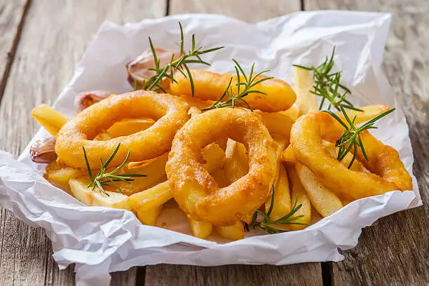 french fries with calamari and rosemary on white paper