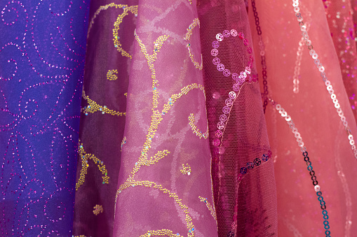 Fancy, sparkly bolts of pink and purple patterned Indian fabrics lined up (close-up).