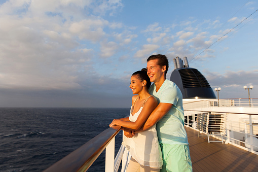 cheerful young couple looking at sunrise on cruise ship