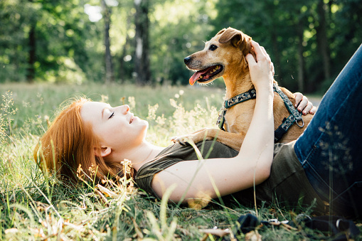 young woman Lying On Back in grass and playing with her small Mixed-breed dog