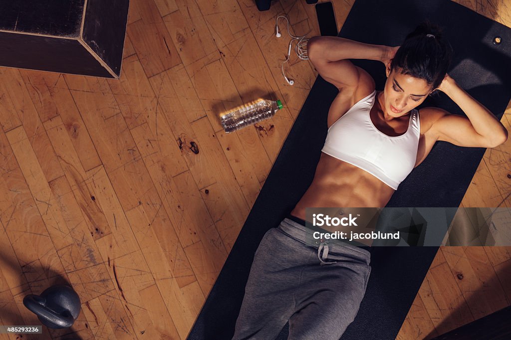Muscular woman doing sit-ups in gym Muscular woman doing sit-ups while lying on the floor. Overhead shot of female model doing stomach exercise in gym. Aerial View Stock Photo