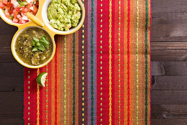 an overhead close up shot of a colorful placemat and bowls with a variety of dips.