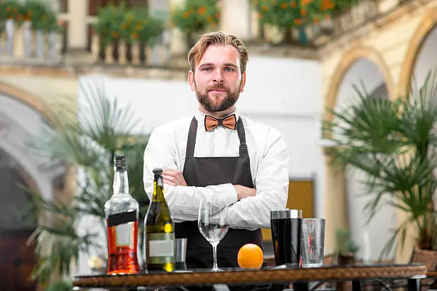 Portrait of handsome barman in uniform with bottles and shaker at the restaurant 