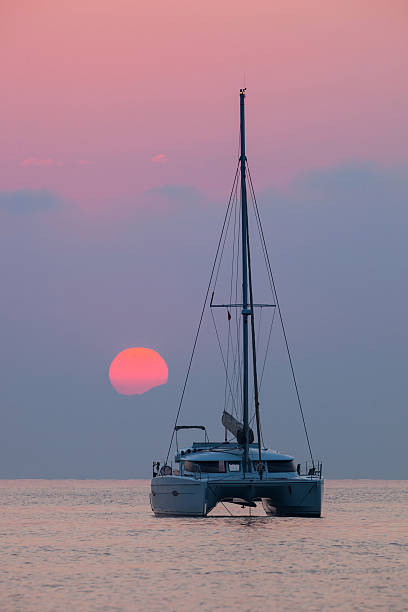 Sailing catamaran on background of beautiful sunset in the sea stock photo