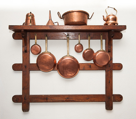 Different kind of vintage copper cookware, pans, coffee pot and funnel hung on wooden shelf in kitchen