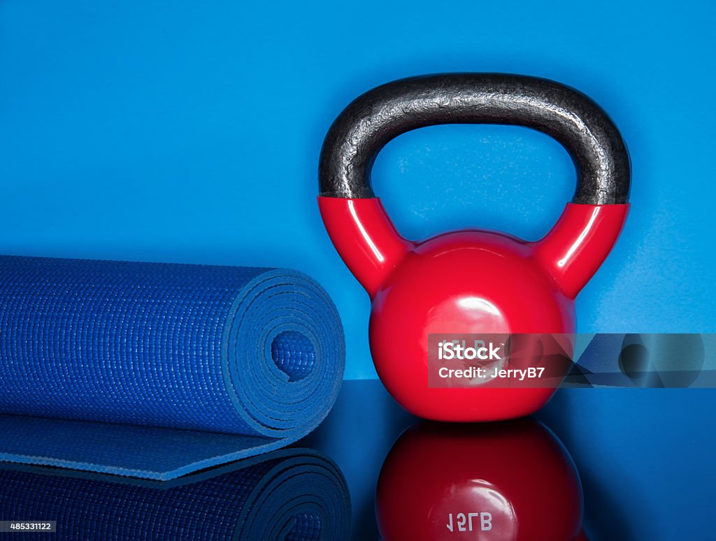 Kettle Ball Workout Red Kettle ball on blue background with mat roll Exercise Mat Stock Photo