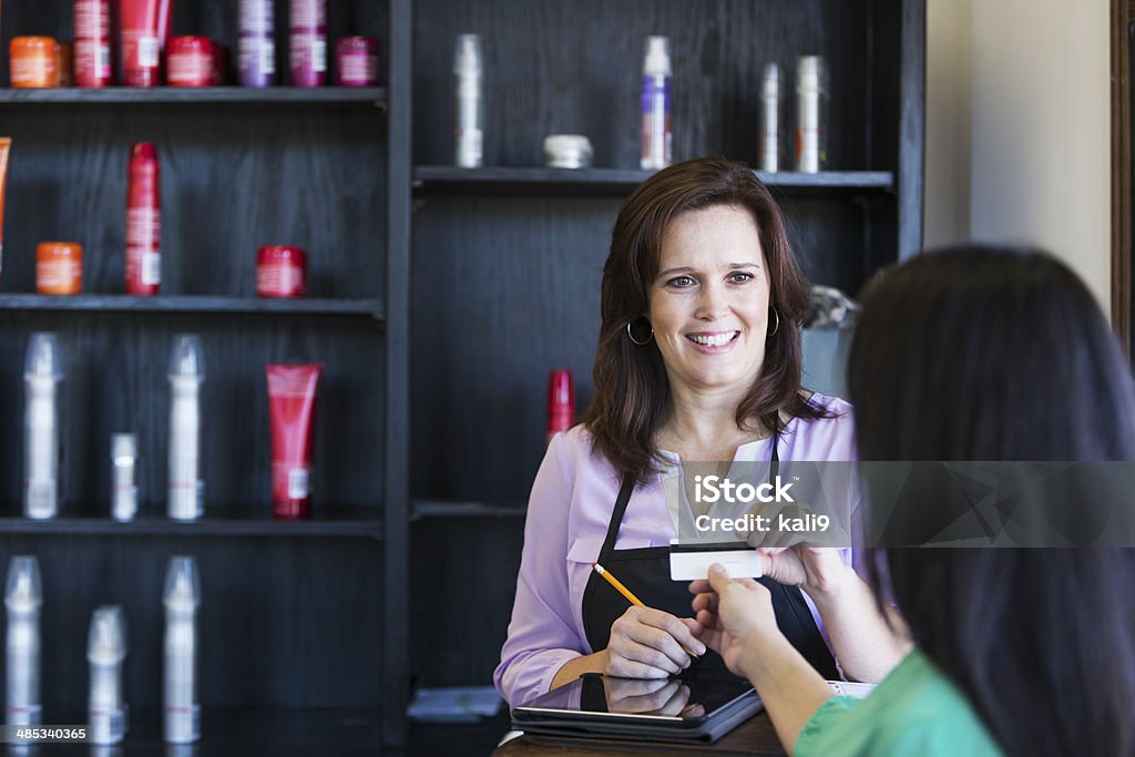 Saleswoman taking credit card from customer Saleswoman (30s) taking credit card payment from customer. Hair Salon Stock Photo