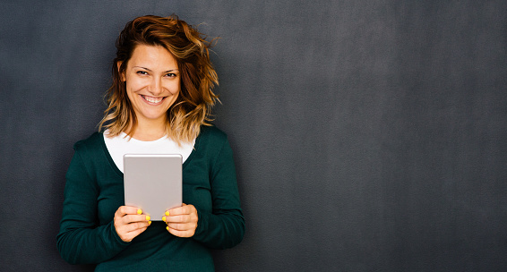 Woman holding a tablet in front on blackboard