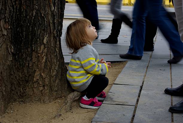 Little girl with ponytail and overalls sitting on a bench in a playground.