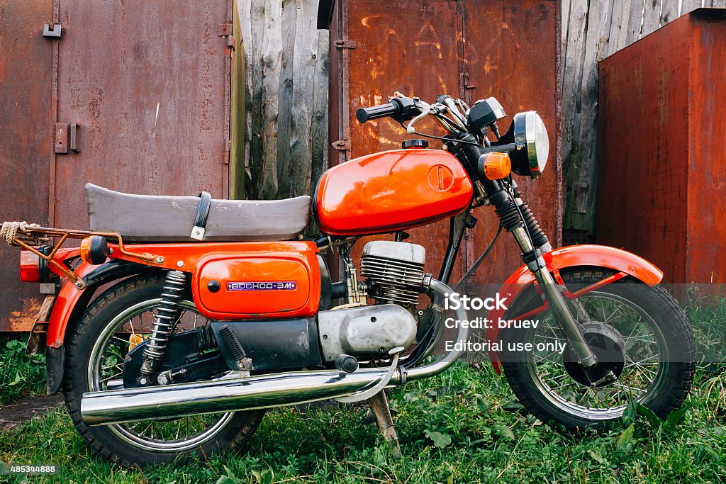 Vintage Red Motorcycle Generic Motorbike In Countryside Minsk, Belarus - September 22, 2013: Old Red Russian (Soviet) Motorcycle Parked On Green Grass Yard. This motorcycles produced at Degtyarev plant in Russian town Kovrov since 1965. Motorcycle Stock Photo