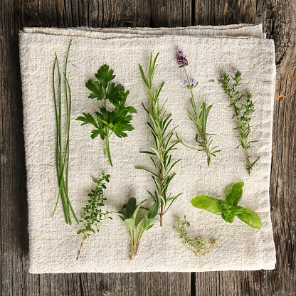 A still life featuring kitchen herbs on a cloth and old wood.