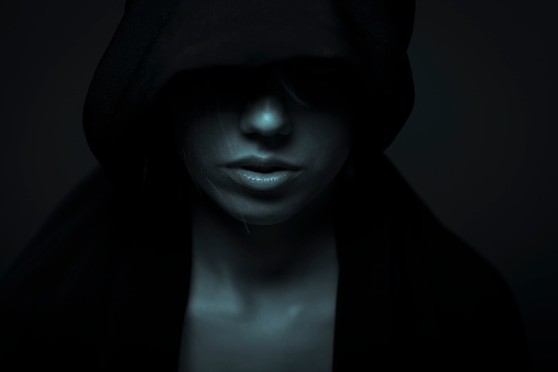 Low key portrait of a young woman in black hood. Toned image