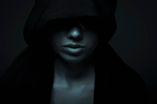 Portrait Of Woman In Darkness Low key portrait of a young woman in black hood. Toned image woman alone dark shadow stock pictures, royalty-free photos & images