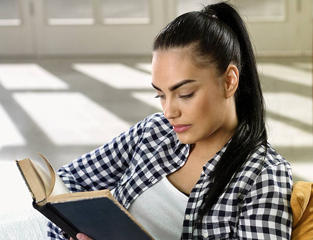 istock Young woman on sofa reading a book 485357618