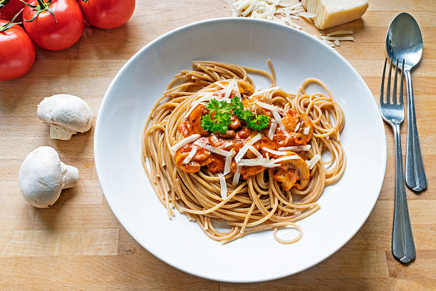 wholemeal spaghetti with sauce of tomatoes, mushrooms and parmes rustic wholemeal spaghetti with sauce of tomatoes, mushrooms and Parmesan cheese on a wooden table whole wheat stock pictures, royalty-free photos & images