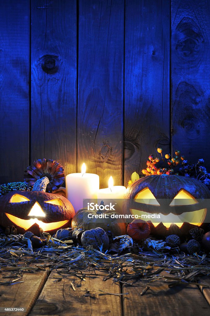 halloween pumpkins illuminated halloween pumpkins, candles, nuts, maize-cob and apple on straw in front of old weathered wooden board in blue sunset light 2015 Stock Photo