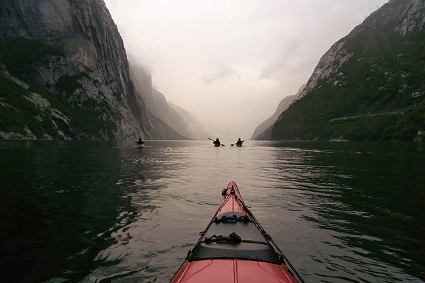 View from a red kayak in the Lysefjord in Norway during twilight at the end of a cloudy and misty day. Lysefjord or Lysefjorden is a fjord located in Forsand in Ryfylke in south-western Norway east of the city of Stavanger. It is a popular fjord to visit for tourists and famous for the rock of Preikestolen and the Kjeragbolten.