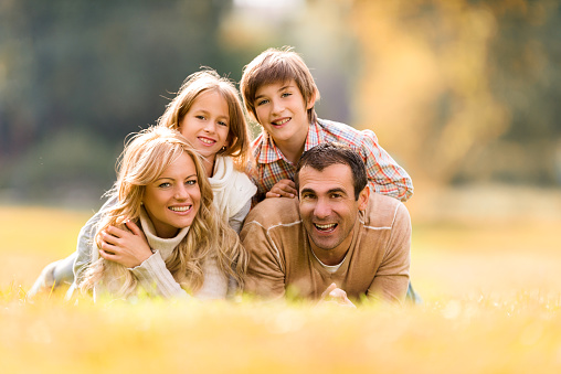 Portrait of a young affectionate family hugging and standing in nature near forest while smiling at the camera. A cheerful family of four is standing in nature and hugging while posing and smiling.