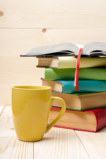 Stack of colorful books and cup on wooden table. Back to school. Copy space