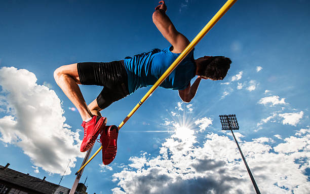 Low angle view of a young man performing high jump. Male athlete performing high jump against the sky. high jump stock pictures, royalty-free photos & images