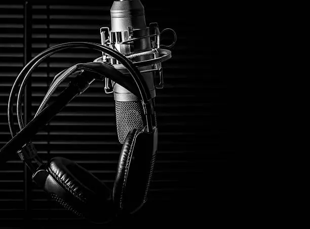 Photo of condenser microphone on boom stand with headphones, in dark studio