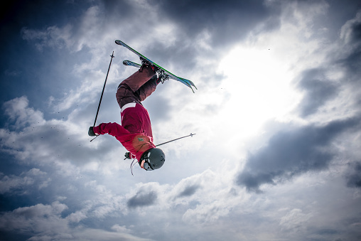 Man backflipping upside down mid air whilst freestyle ski jumping.