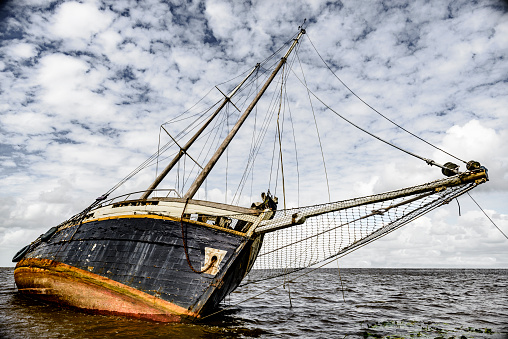 Stranded shipwreck of an old sailing boat. The boat is leaning on its side and is badly damaged.