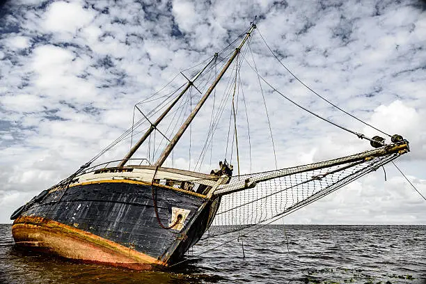 Stranded shipwreck of an old sailing boat. The boat is leaning on its side and is badly damaged.