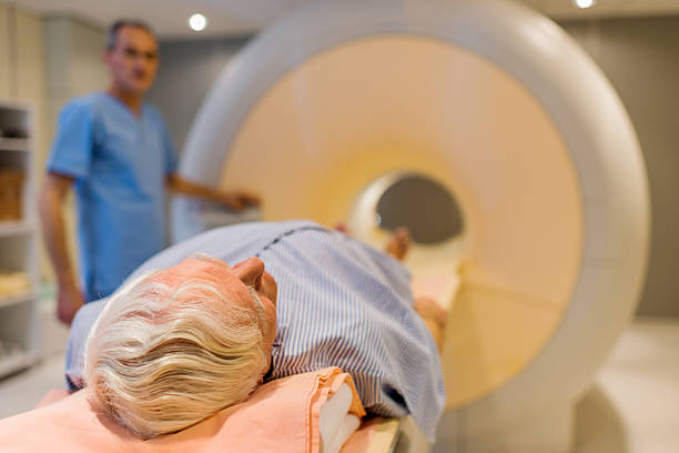 Senior patient about to receive an MRI scan. Senior male patient lying down at MRI scan. Radiologist is in the background. pet scan photos stock pictures, royalty-free photos & images