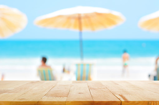 Wood table top on blurred background of people relaxing at the beach - can be used for montage or display your products