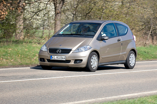 Wiesbaden, Germany - April 2, 2011: A senior couple in a gold-metallic Mercedes-Benz A-Class (W169 facelift) driving on a country-road near Wiesbaden (Germany) on a warm spring day. Mercedes-Benz A-Class-cars (also known as W169-series) are mini MPV cars, the first generation started in 1997. Mercedes-Benz is a German manufacturer of automobiles and trucks and a division of Daimler AG, formerly Daimler-Chrysler