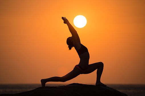 Warrior pose from yoga by woman silhouette on sunset