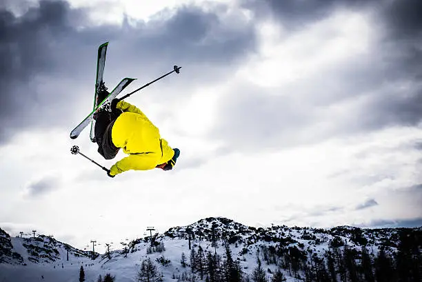 Man backflipping upside down mid air whilst freestyle ski jumping.
