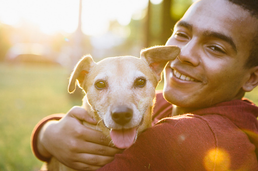 portrait of a young man hug his small Mixed-breed dog, looking at camera 