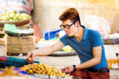 Young Vietnamese man picks up fresh apricots at Hanoi street market. He is smiliing while choosing the best fruit. Photographed in Hanoi Vietnam.